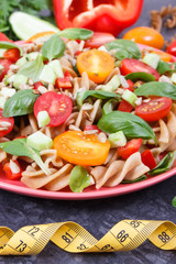Tape measure and salad with wholegrain pasta and vegetables as healthy meal containing vitamins and minerals