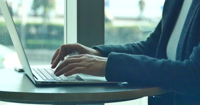 4k silhouette of female working on laptop computer in coffee shop desk,city pedestrian and traffic window view,business correspondence using a laptop,keyboard input,write article,writing report.