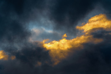 Stunning fluffy thunderstorm clouds illuminated by disappearing rays at sunset and dark thunderclouds floating across sky to change season weather. Natural abstract meteorology background.