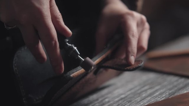 Close-up: leather processing and product manufacturing using an automatic tool. An unknown tanner works in a workshop, only hands in the frame. Handmade process with special equipment. Slow motion