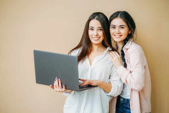 Young smiling girls students in casual with laptop in hands isolated on beige background