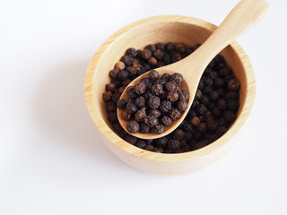 Above of black pepper seeds in wooden bowl isolated on white background.