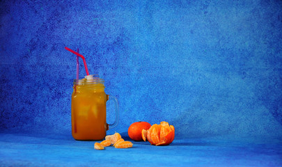 Glass mug of citrus juice with ice and slices of ripe mandarin next to a blue background. © Алексей Желтухин