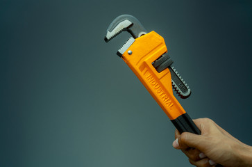 Plumber hand holding handle of chrome pipe wrench isolated on dark background. Metal monkey wrench...