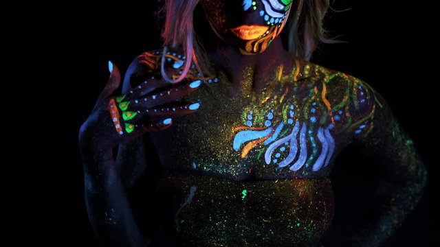 Sexual Body of Young Bodyarted Avatar Girl in Ultraviolet Light. Face of Fashion Model under UV Black Lamp. Colored Dots on the Shoulders, Patterns on the Chest. Colorful Make up. Ghost or Alien.