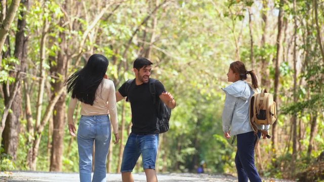 HD Slow Motion group of happy friends Asian woman and man hiking with backpack on forest dirt road in summertime. Three friends enjoy explore walking with smiling, laughing and talking together
