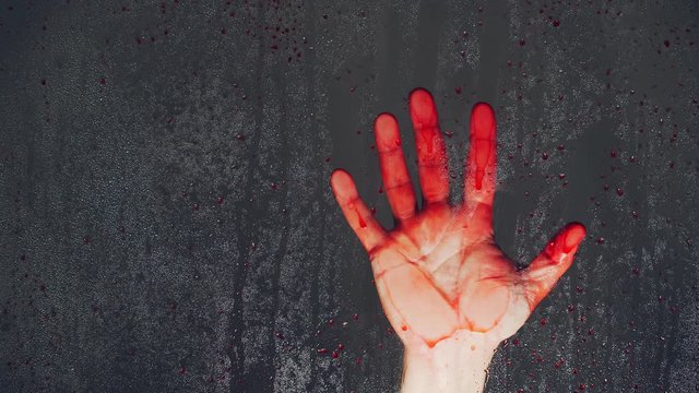 The bloody men's hand on the wet window with red drops. The theme of murder and violent death. Close-up