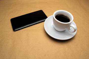 Fototapeta na wymiar White cup with coffee mobile phone on a beige background
