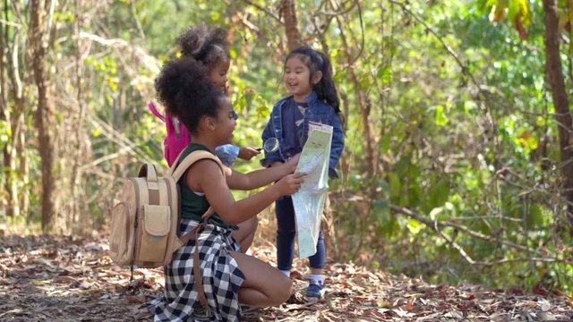 HD Slow Motion group of happy pretty little girl hiking together with backpacks on forest dirt road and looking at the map for exploring the forest. Three kids having fun adventuring in summer day.