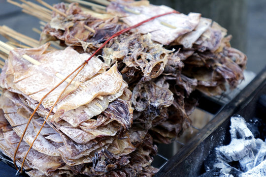 Daing na Pusit or dried squid on barbecue sticks grilled over charcoal