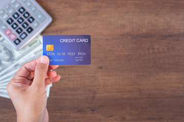 Close-up of hand holding a blue credit card with money US dollars background and a calculator...