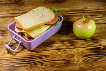 Lunch box with sandwiches and apple on a wooden table