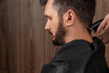 Obraz premium The master makes a haircut to the client with an electric machine, trimmer, close-up. The process of male haircuts at the hairdresser, barbershop. Body care, lifestyle, metrosexual.