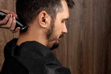 Obraz premium The master makes a haircut to the client with an electric machine, trimmer, close-up. The process of male haircuts at the hairdresser, barbershop. Body care, lifestyle, metrosexual.