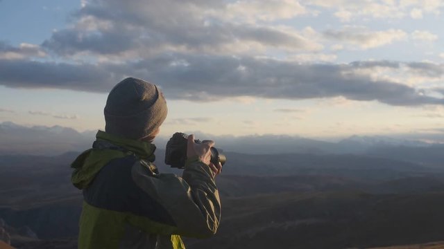 Close up: tourist photographer takes photos of mountains and valley at sunset, epic horizontal view. Hiker traveler holds a professional camera in his hands