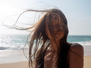 Portrait of a young woman with tangled hair from the wind against the background of the ocean