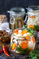 Pickled cauliflower with carrots in a glass jar on a dark wooden table. Fermented food.