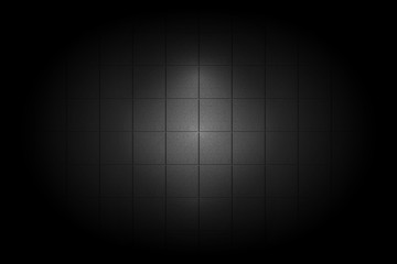 Light shining down on black ceramic tile wall in dark room with copy space, abstract background
