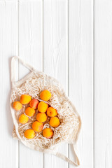 Textile eco bag with fruits on white wooden background top-down copy space