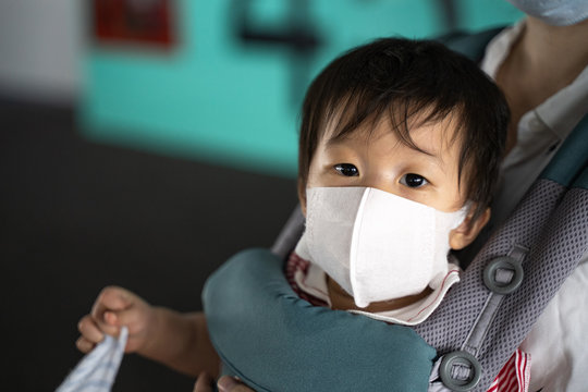 Asian baby with mother in baby carry,baby is wearing a protection mask against air pollution and Wuhan covic corona virus before flight in terminal DonMuang airport,Bangkok, Thailand.