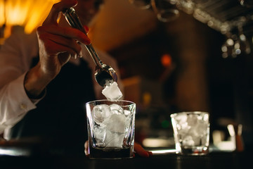 The bartender pours ice into cocktail glasses.