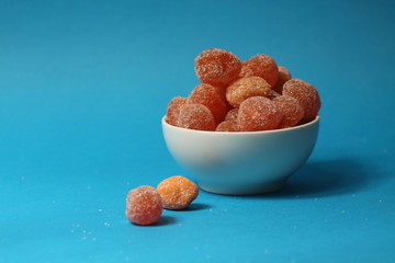 a bowl of kumquat coated with sugar isolated on blue background