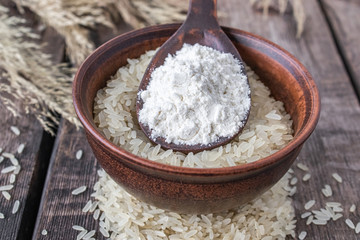 White rice in a bowl with a spoon of white flour on a background of old boards. Jasmine rice for cooking.