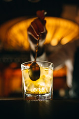 The bartender stirs a spoonful of whiskey with ice in a glass.