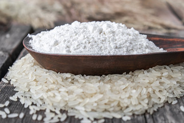 Rice flour in a bowl on a pile of white rice on old boards.