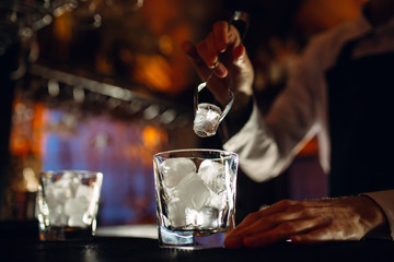 The bartender pours ice into cocktail glasses.