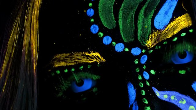 Super Closeup of Female Painted Face. UV Powder, Fluorescent Pigment on Skin. Ultra Violet Blue Eye Lenses. Halloween party, Disco Night Club, Futuristic, Shows and Music concept.