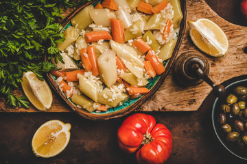 Flat-lay of Turkish traditional leek, rice and carrot meze dish woth lemon on wooden board over rusty dark background, top view. Middle East oriental vegetable appetizer. Vegan and vegetarian food