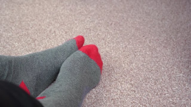 Feet in red-grey socks on a light brown carpet rub against each other