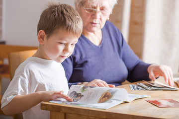 Portrait of beautiful mature woman (80 years old) with her great-grandson at home, reading...