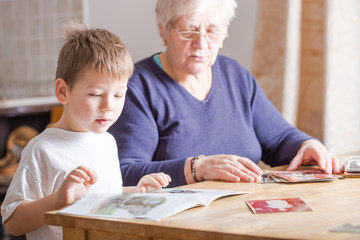 Portrait of beautiful mature woman (80 years old) with her great-grandson at home, reading...