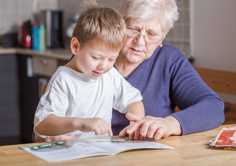Portrait of beautiful mature woman (80 years old) with her great-grandson at home, reading...
