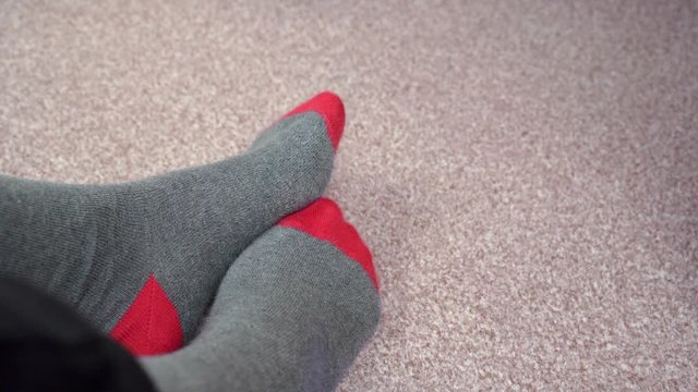 Feet in red-grey socks on a light brown carpet rub against each other