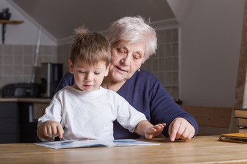 Portrait of beautiful mature woman (80 years old) with her great-grandson at home, reading...