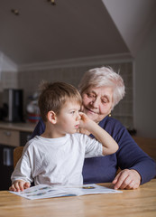 Portrait of beautiful mature woman (80 years old) with her great-grandson at home, reading...