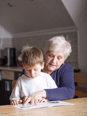 Portrait of beautiful mature woman (80 years old) with her great-grandson at home, reading...