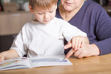 Portrait of beautiful mature woman (80 years old) with her great-grandson at home, reading educational book together
