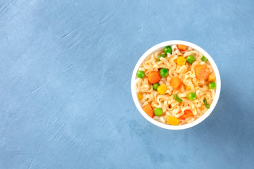 Ramen cup, instant soba noodles with carrot and green peas in a plastic cup, top shot with copy space