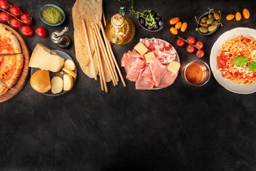 Italian food with a place for text, a flat lay design template for a restaurant. Pizza, pasta, cheese, ham, wine, olives, pesto, capers, olive oil, tomatoes, shot from the top