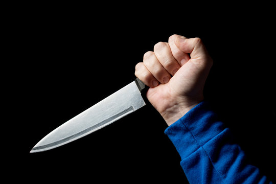 A kitchen knife in the man&rsquo;s hand is brought in for a strike. Close-up on a black background