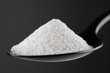 collagen powder in black spoon. grey background closeup. Natural beauty and health supplement