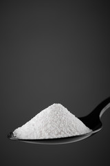 collagen powder in black spoon. grey background closeup. Natural beauty and health supplement