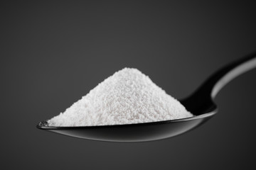 collagen powder in black spoon. grey background closeup. Natural beauty and health supplement