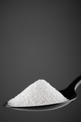 collagen powder in black spoon. grey background closeup. Natural beauty and health supplement