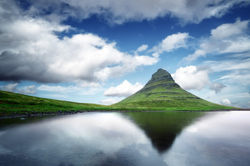 Picturesque landscape with Kirkjufell mountain, clear lake and cloudscape in blue sky