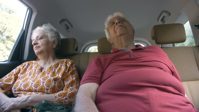 Old Indian couple sleeping in the back seat of a moving car - senior lifestyle concept. Low angle shot of tired male and female taking a power nap while riding back home in a car from a city market...